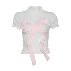 A ribbed knit top with an oversized ribbon bow applique, available in black and white, styled for a chic and modern look.

